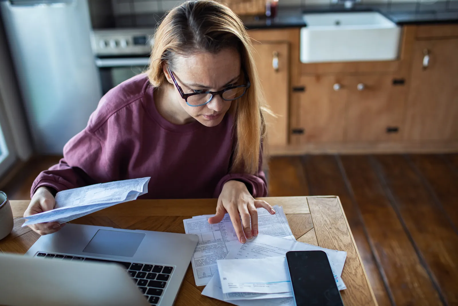 Woman reviewing household bills and paperwork at a kitchen table