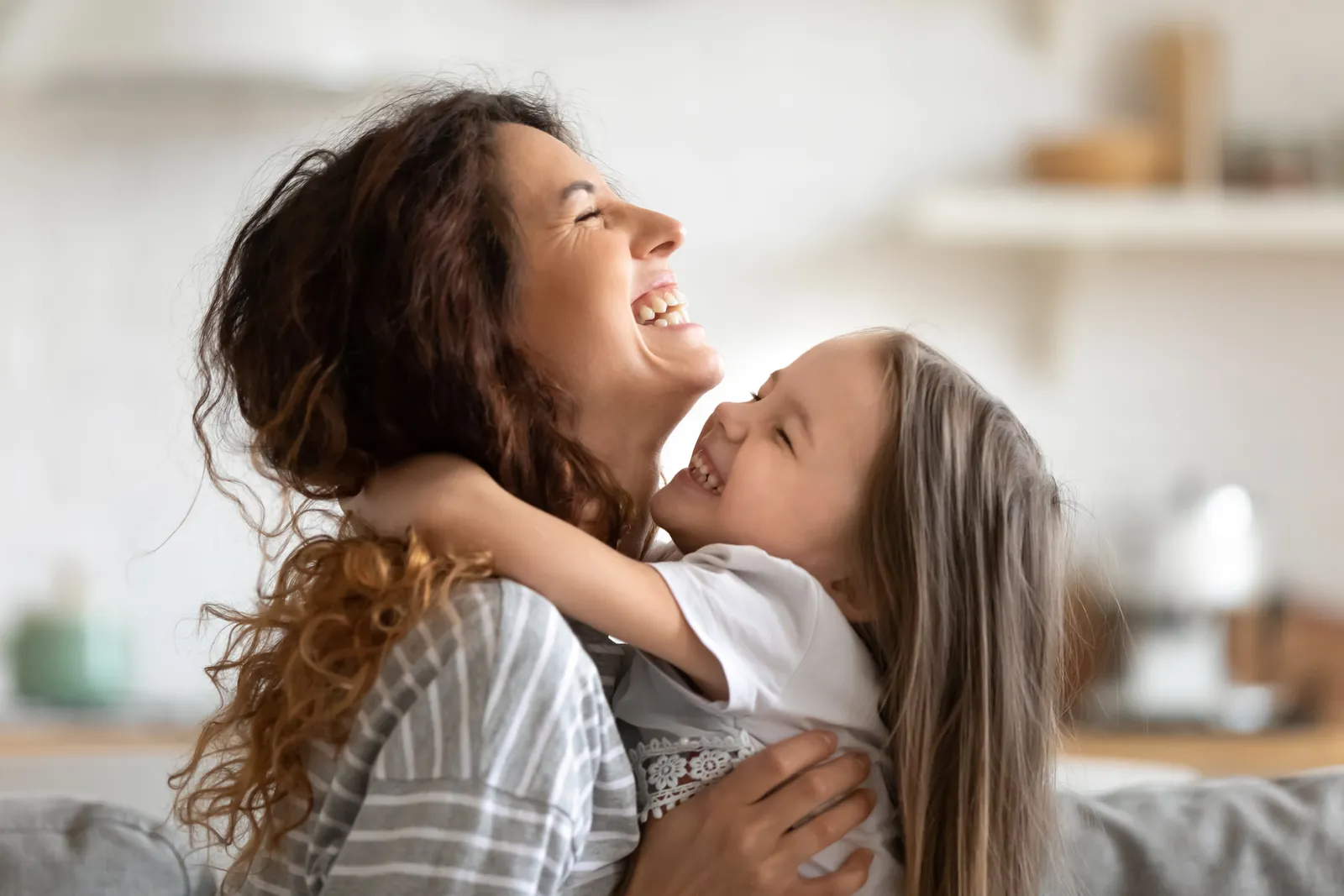 Mother and young daughter laughing and embracing at home