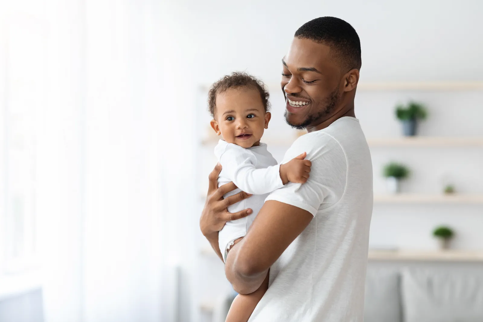 A smiling father holding his baby in a bright, airy room